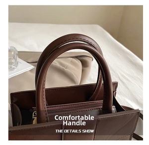 Detailed close-up of dark brown leather handbag handle and golden zipper hardware