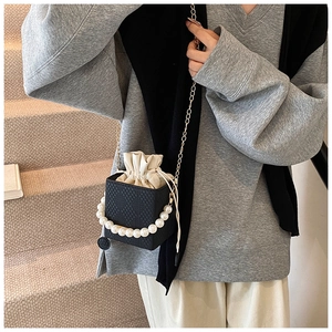 Detail of black woven bucket bag with pearl handle and drawstring pouch on a model