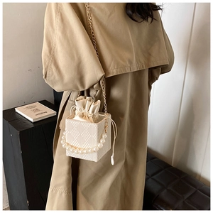 Detail of quilted bucket bag with pearl handle and golden chain strap in white