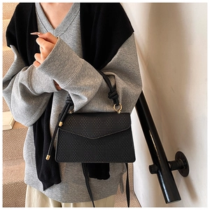 Detail of black woven leather crossbody bag with gold ring and knot handle on model