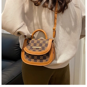 Detail of a brown leather saddle bag with vintage check pattern and metal hardware