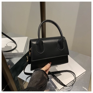 Detail of a black matte textured crossbody bag with a top handle and metallic hooks