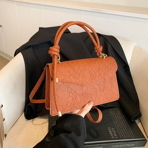 Fashionable warm orange-brown handbag with delicate lace embossed leather on a white chair
