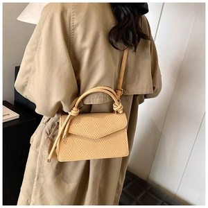 Detail of yellow crossbody bag with knot handle and woven texture worn with a trench coat