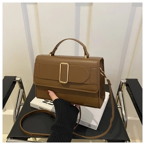 Detailed close-up of brown textured leather crossbody bag with golden metal buckle clasp