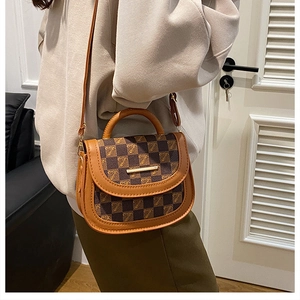 Detail of a brown checkered saddle bag featuring a gold metal bar and adjustable strap