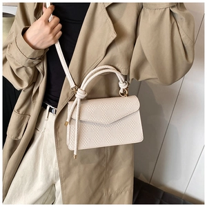 Detail of beige woven square crossbody bag with twisted handle and gold hardware