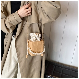 Detail of beige bucket bag featuring large pearl handle and metal chain strap