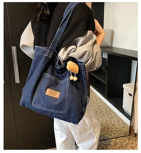 Detail of dark blue denim tote bag with brown leather logo and cute teddy bear charm