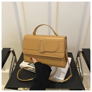Detail of khaki leather square handbag with gold buckle held against a minimalist background