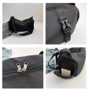 Detail of black cylinder crossbody bag showing wide strap, plastic buckle and metal zippers