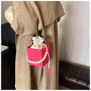 Close-up of fuchsia woven bucket bag with pearl handle and golden chain strap