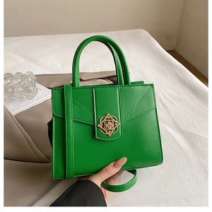 Détail du sac à main en cuir vert avec boucle trèfle dorée sur un tissu texturé