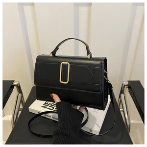 Close-up of minimalist black matte handbag with large gold buckle and slim top handle