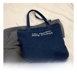Detail of dark blue denim tote bag featuring white embroidered 'Less Mondays' text