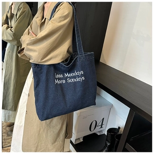 Detail of dark blue denim tote bag featuring white embroidered Less Mondays More Sundays text