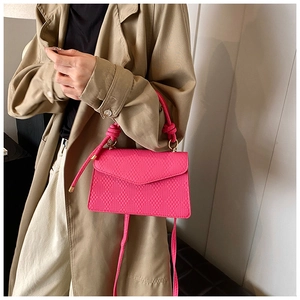 Detail of rose red textured leather crossbody bag with knot handle and gold hardware