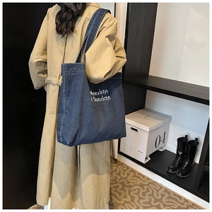 Mannequin portant un sac cabas en denim bleu foncé brodé avec une large bandoulière