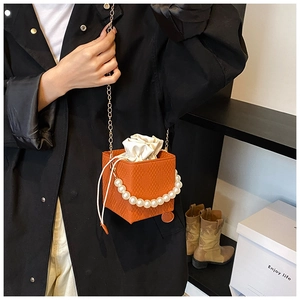 Moderna borsa a cubo intrecciata arancione con perle e catena dorata sulla modella