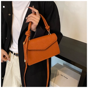 Detail of orange woven texture handbag with golden hardware and unique knot handle