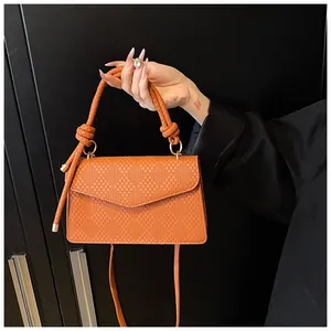 Detailed close-up of orange woven texture crossbody bag with knotted handle and flap closure