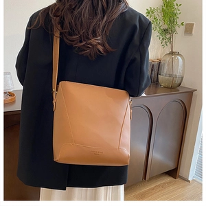 Detail of brown leather bucket bag showing stitched bottom and embossed fashion text