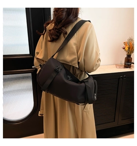 Detail view of a black nylon cylinder crossbody bag with adjustable wide strap on model