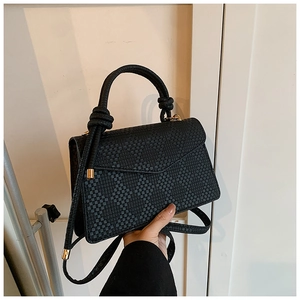 Close-up of woven texture detail on black crossbody bag with gold hardware and flap
