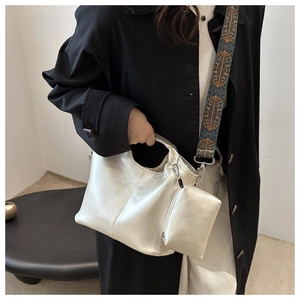 Detail of silver tote bag with textured surface and patterned woven crossbody strap