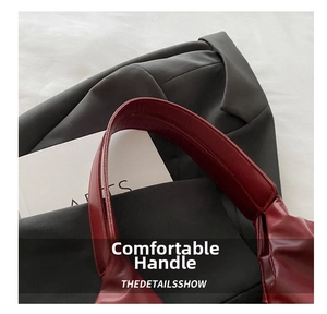 Detailed close-up of wide red leather handles and neat stitching on a luxury tote bag