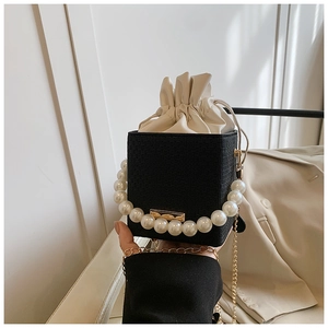 Detail of black woven bucket bag with large pearl handle and golden chain strap