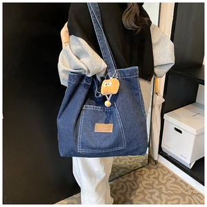 Detail of blue denim tote bag with leather logo tag and brown monster plush charm