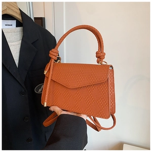 Detail of caramel brown woven leather crossbody bag with elegant gold hardware