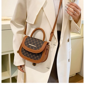 Detail of a brown patchwork saddle bag with gold metal trim and smooth leather handle