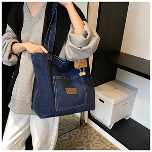 Détail du grand sac cabas en denim bleu avec patch logo en cuir et charme monstre en peluche