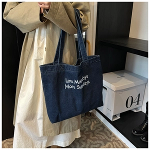 Close-up of deep blue denim tote bag with white 'Less Mondays More Sundays' embroidery