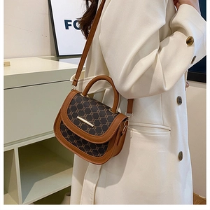 Detail of vintage brown monogram saddle bag with golden bar buckle on white suit