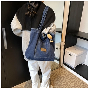 Detail der blauen Denim-Tragetasche mit Vordertasche und Lederlogo am Schultergurt