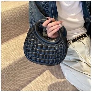 Detail of black faux leather handbag with crocodile pattern held by model on stairs