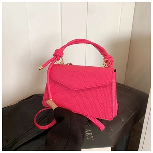 Detail of hot pink woven crossbody bag with knotted handle and gold hardware on leather