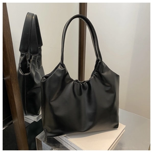 Detail of black glossy tote bag with pleated top design resting on a mirror surface