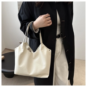 Close-up of minimalist cream white large PU leather tote bag worn as an underarm shoulder bag
