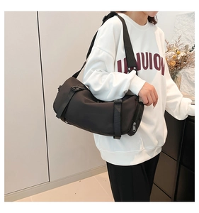 Detail of black cylinder messenger bag featuring adjustable straps and plastic buckles
