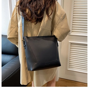 Detail of minimalist black leather bucket bag with embossed logo and wide shoulder strap