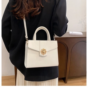 Détail d'un sac à main en cuir blanc crème avec boucle fleurie dorée et poignée ronde