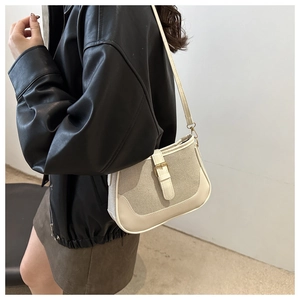 Detailed side view of beige canvas and leather shoulder bag with vintage metal buckle strap