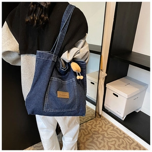 Detail einer großen Denim-Einkaufstasche mit Lederaufnäher und Plüschanhänger