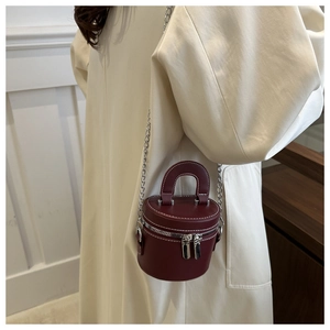 Detail of wine red mini cylinder bag with silver chain strap on white coat