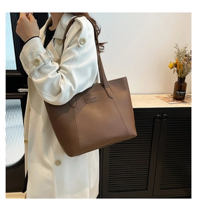 Détail du sac cabas en simili cuir marron montrant les fines anses et l'emblème mode