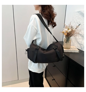 Rear view of model wearing a large black nylon sports crossbody bag with buckle straps